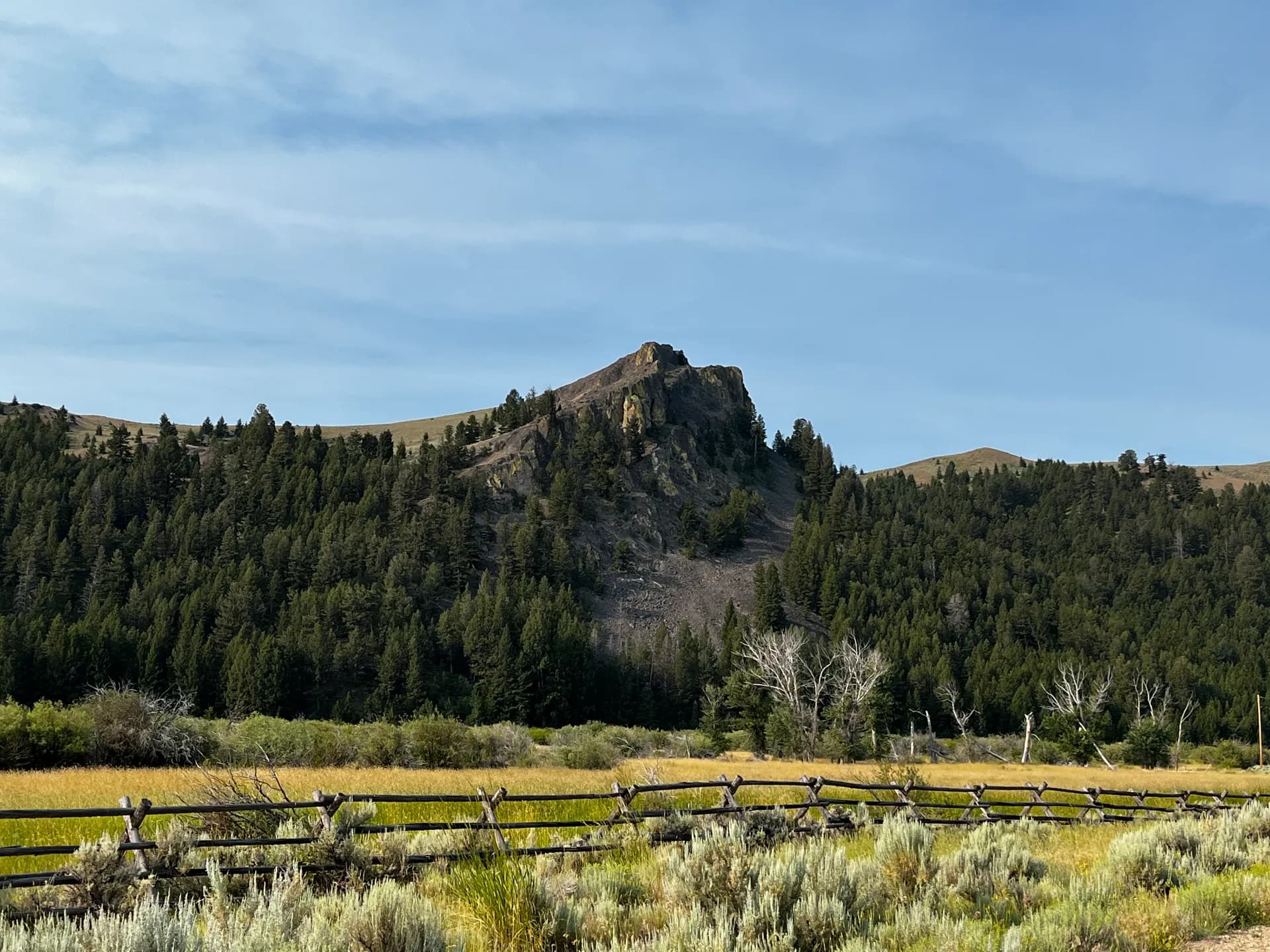 Rocky peak above a summer meadow and split-rail fence